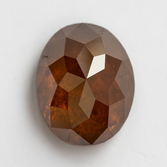Face-up macro of the oval reddish-orange diamond on white, showing broad geometric facets and visible internal patterning.