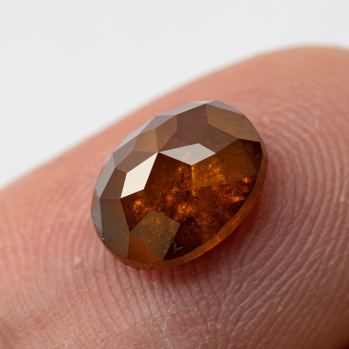 Face-up fingertip view of the oval stone with a bright central reflection and warm orange-brown body.