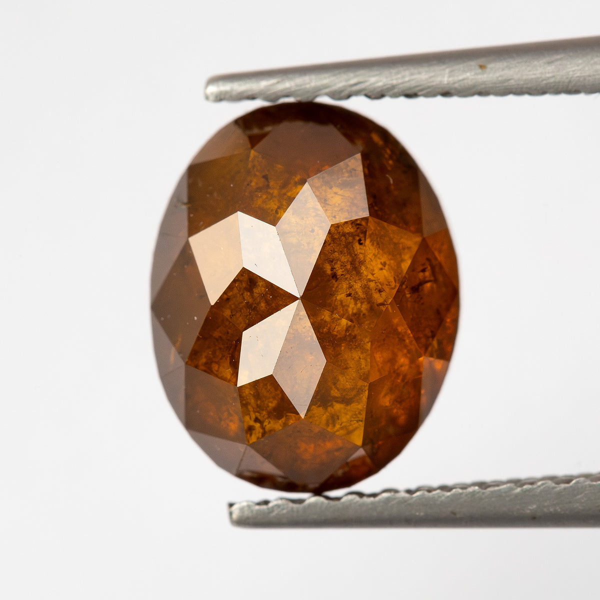 Front-facing tweezer view of the oval reddish-orange diamond, showing the full outline and warm brown-orange reflections.