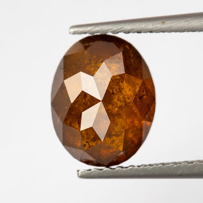 Front-facing tweezer view of the oval reddish-orange diamond, showing the full outline and warm brown-orange reflections.
