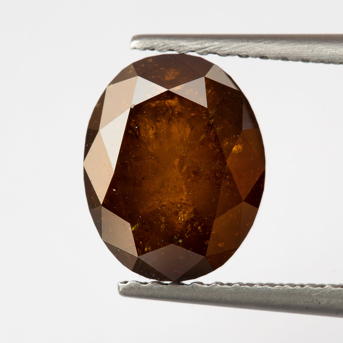Opposite-side tweezer view of the oval stone, showing a broader central facet field.
