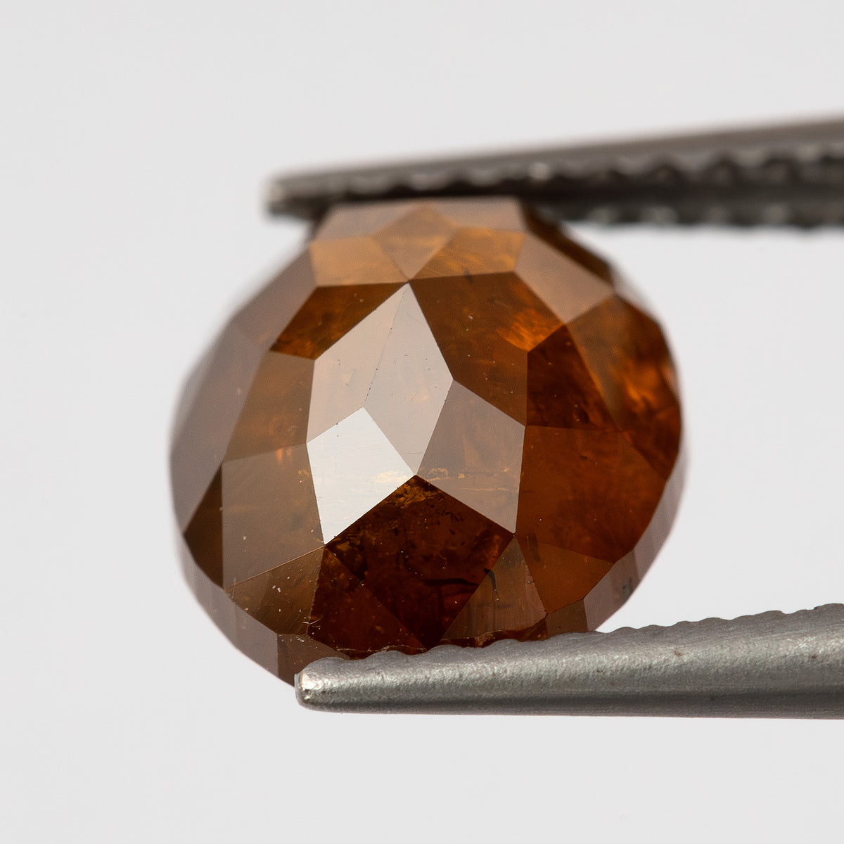 Tweezer-held profile of the oval stone, showing the edge and depth between its faceted sides.