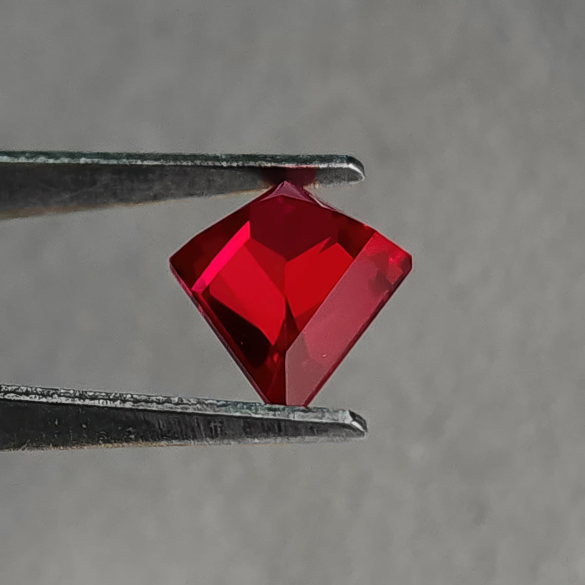 Angled reverse pavilion of a kite-shaped lab-grown ruby in tweezers, showing a raised central facet ridge.