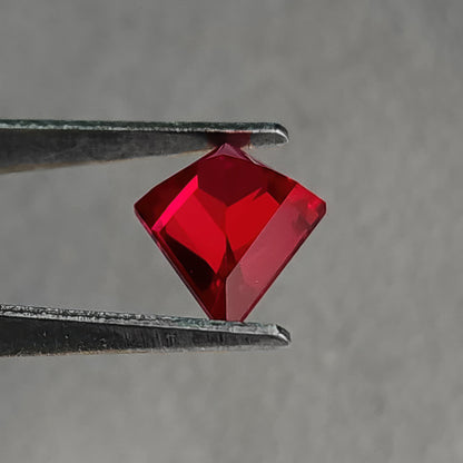 Angled reverse pavilion of a kite-shaped lab-grown ruby in tweezers, showing a raised central facet ridge.