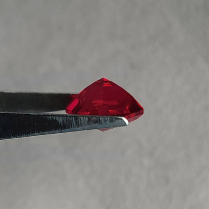Side profile of a kite-shaped lab-grown ruby in tweezers, showing its crown and pavilion depth.