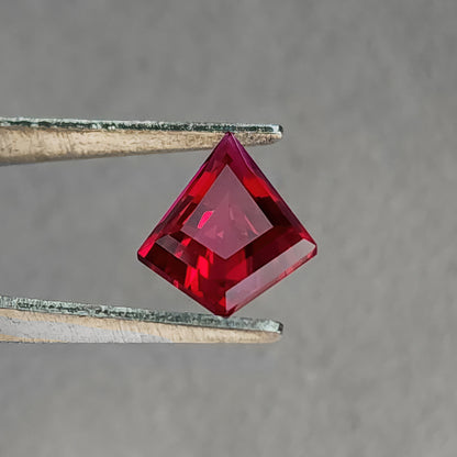 Table-side kite-shaped lab-grown ruby in tweezers, showing a broad pale pink central reflection.