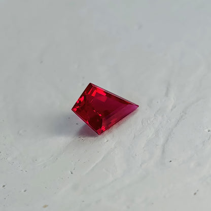 Oblique table-side kite-shaped lab-grown ruby on a white surface, with a dark red flat table, pink border and a shadow.