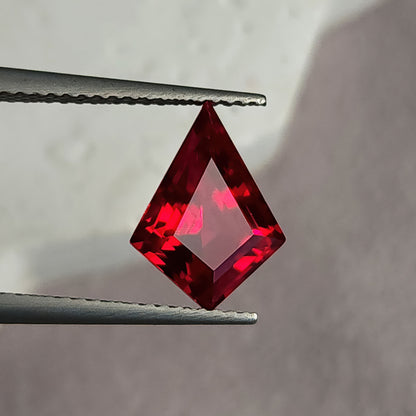 Table-side kite-shaped lab-grown ruby in tweezers against light gray, showing a broad pale pink flat table.