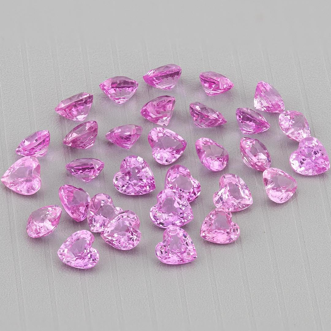 Wider view of the representative pink heart sapphire parcel on gray, showing variations in pink reflections and stone orientation.