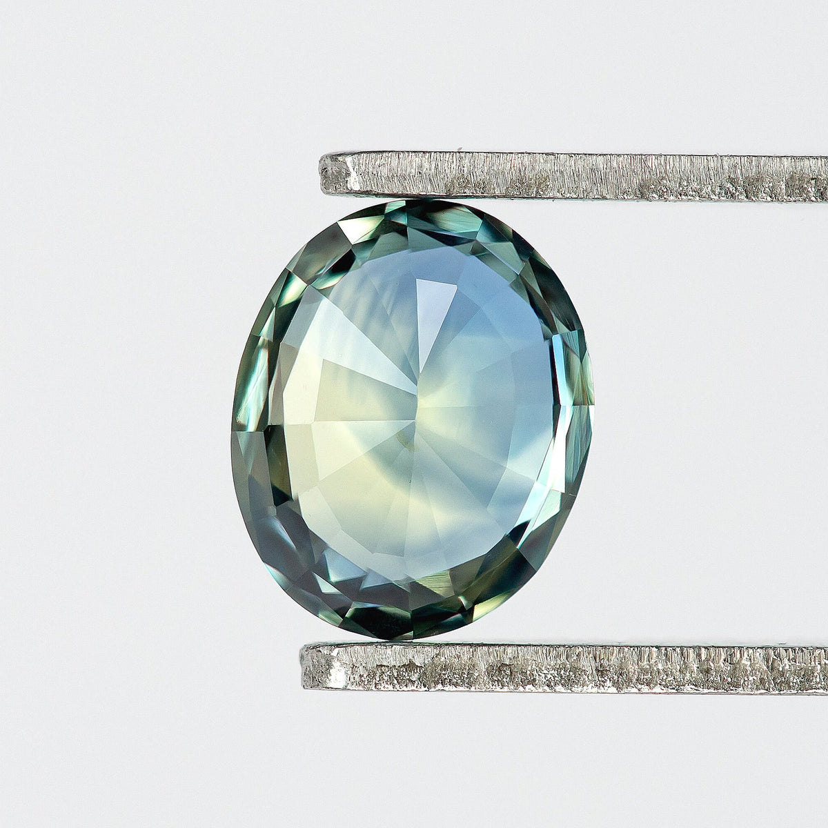 Back view of the oval sapphire in tweezers, with pale blue-green pavilion facets and a darker border.
