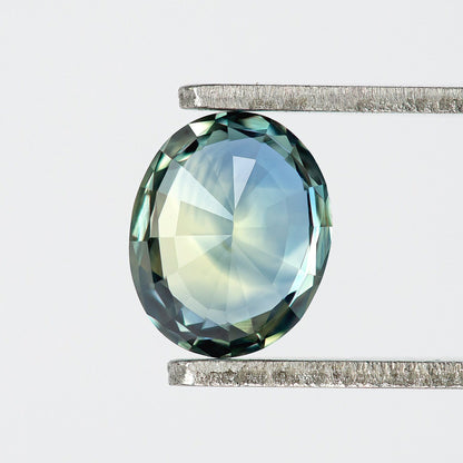 Back view of the oval sapphire in tweezers, with pale blue-green pavilion facets and a darker border.