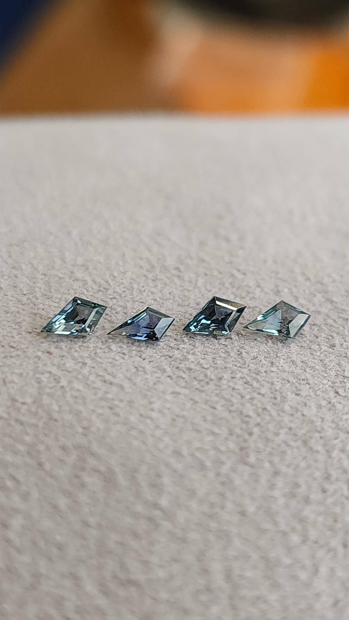 Four kite-shaped teal sapphires tilted face-up, showing changing light reflections. View 6.