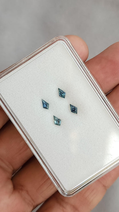 Four kite-shaped teal sapphires shown against a hand for scale. View 3.