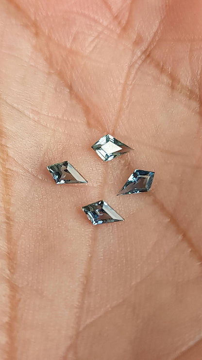 Four kite-shaped teal sapphires shown against a hand for scale. View 4.