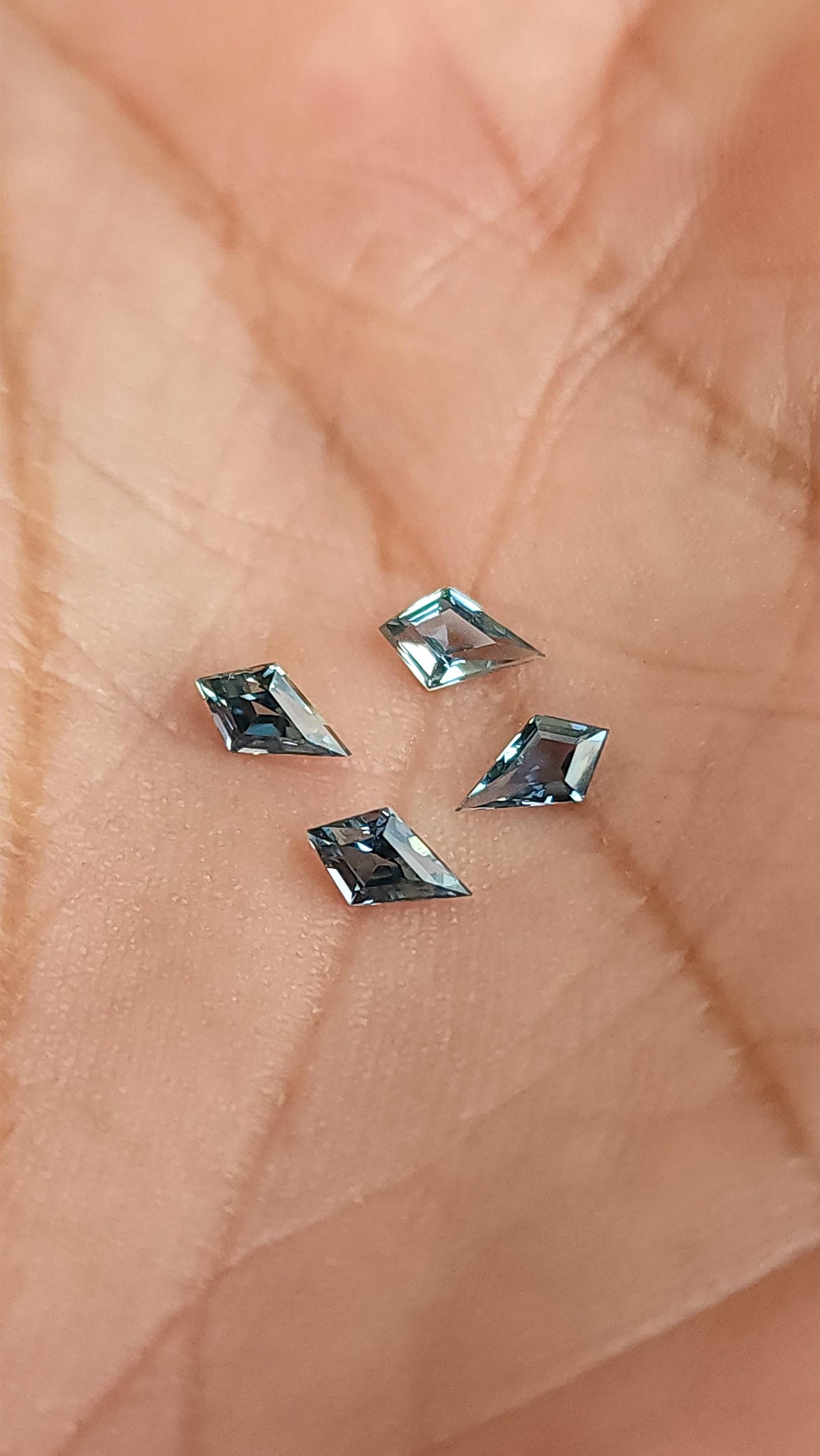 Four kite-shaped teal sapphires shown against a hand for scale. View 5.