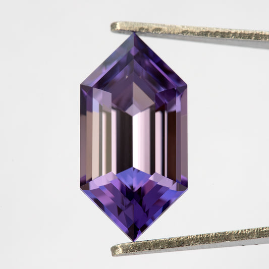 Violet-purple hexagonal lab-grown sapphire held face-up vertically in tweezers against white, with long step facets.