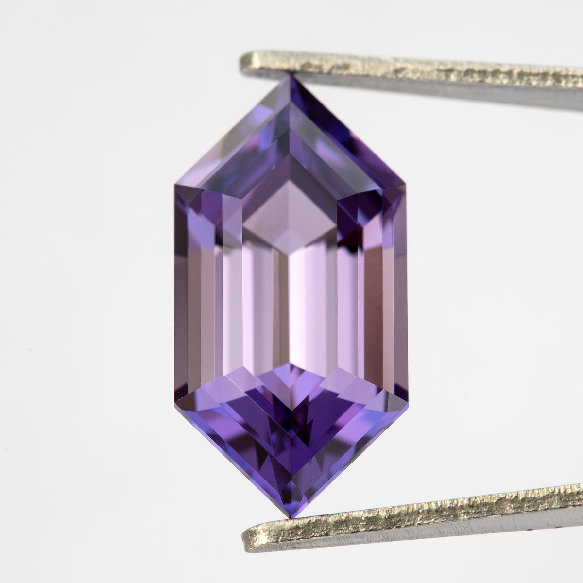 Zafiro hexagonal violeta púrpura visto desde arriba en pinzas con reflejos más claros a través de las facetas escalonadas centrales.