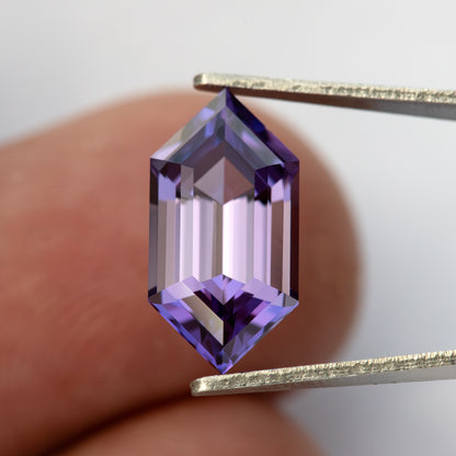 Zafiro violeta púrpura visto desde arriba y sostenido con pinzas contra una yema de dedo para escala.