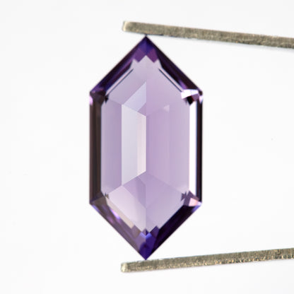 Vista del lado del pabellón del zafiro hexagonal violeta púrpura en pinzas, con amplios reflejos pálidos.