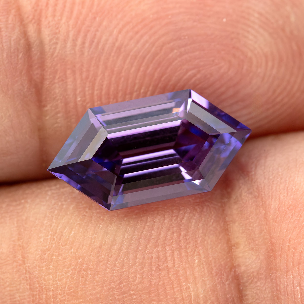 Zafiro de talla escalonada violeta púrpura descansando horizontalmente sobre yemas de dedos, con bandas reflejadas oscuras y pálidas.