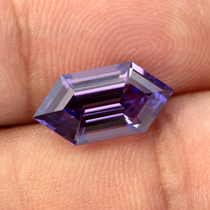 Zafiro de talla escalonada violeta púrpura descansando horizontalmente sobre yemas de dedos, con bandas reflejadas oscuras y pálidas.