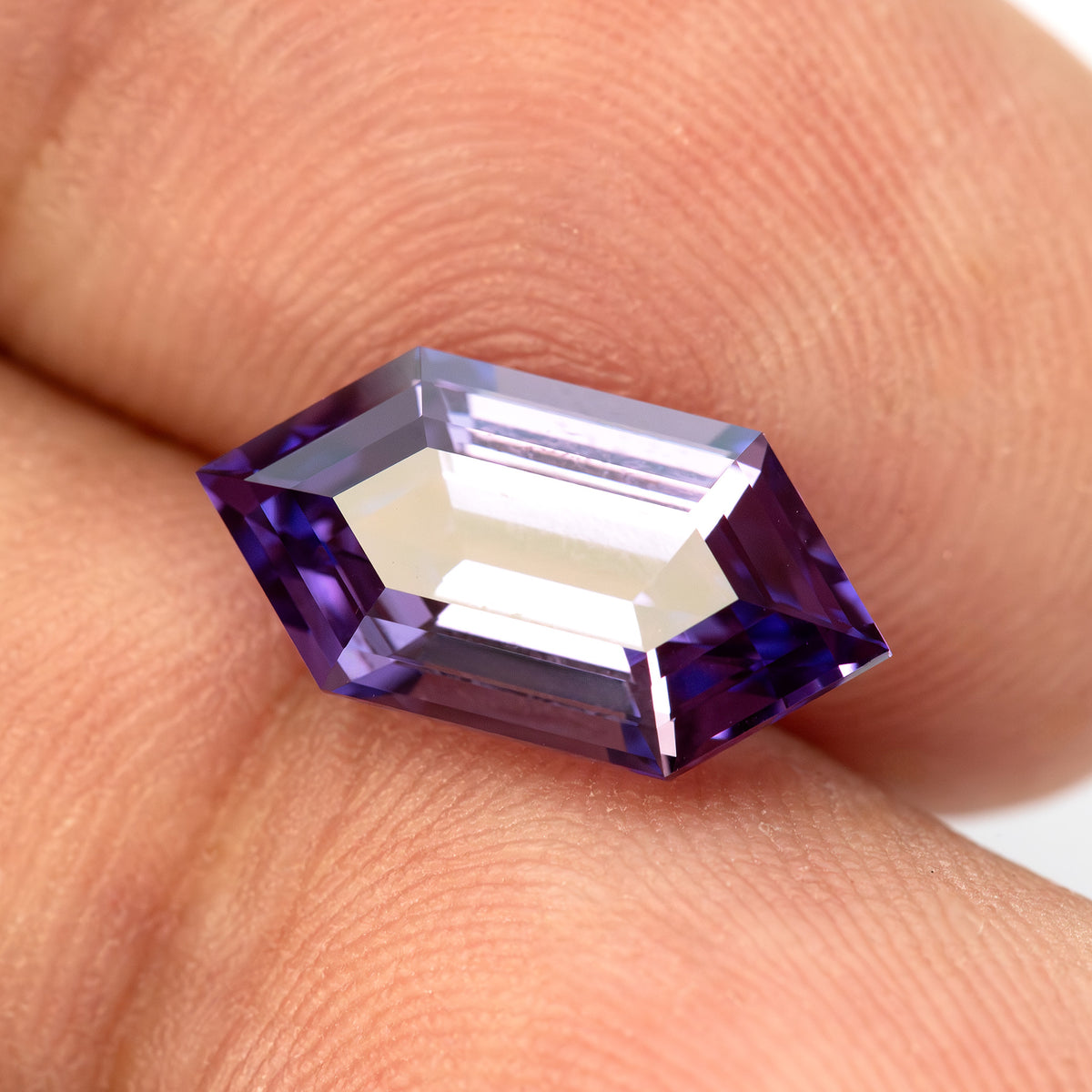 Zafiro hexagonal violeta púrpura sobre yemas de dedos, inclinado de modo que un reflejo brillante cruza la tabla.