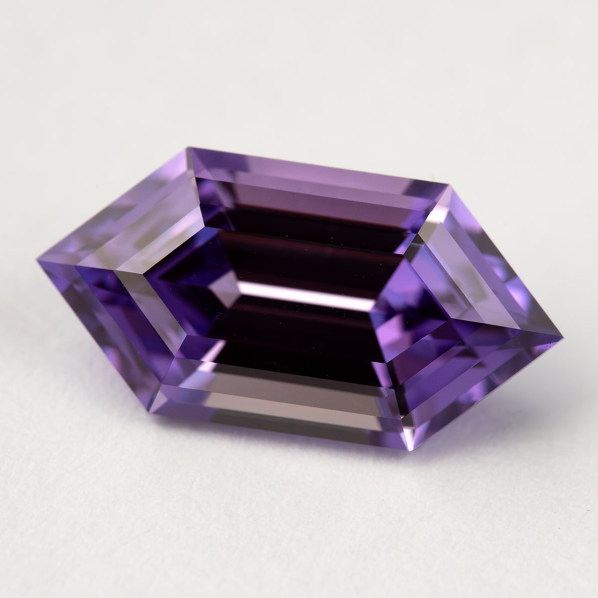 Zafiro hexagonal violeta púrpura visto desde arriba en posición inclinada sobre blanco, con bandas oscuras a través del centro.
