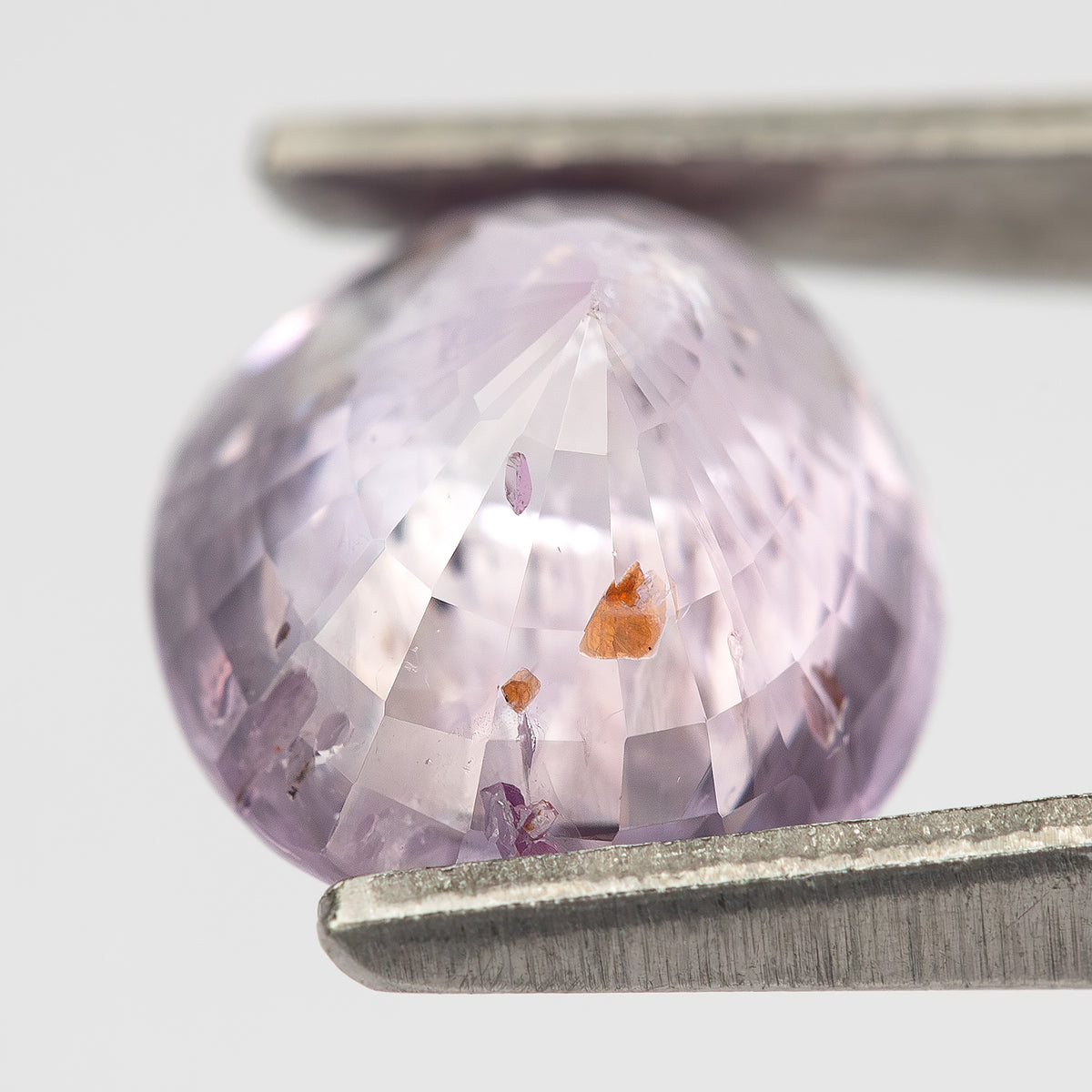 The pink oval sapphire tilted toward the light from the reverse side, showing its depth and brown inclusions.