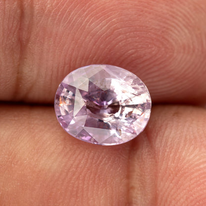 Pink oval sapphire resting face-up on fingertips, with dark and pale reflections across its included interior.