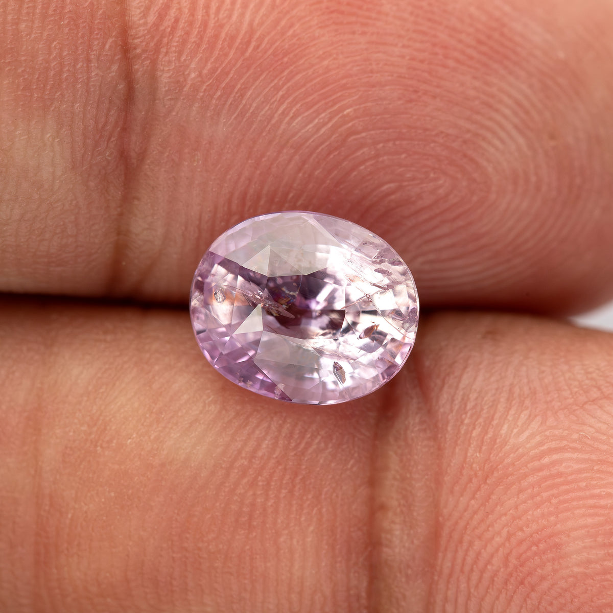 The pink oval sapphire shown smaller on fingertips, giving a wider view of its scale against the skin.