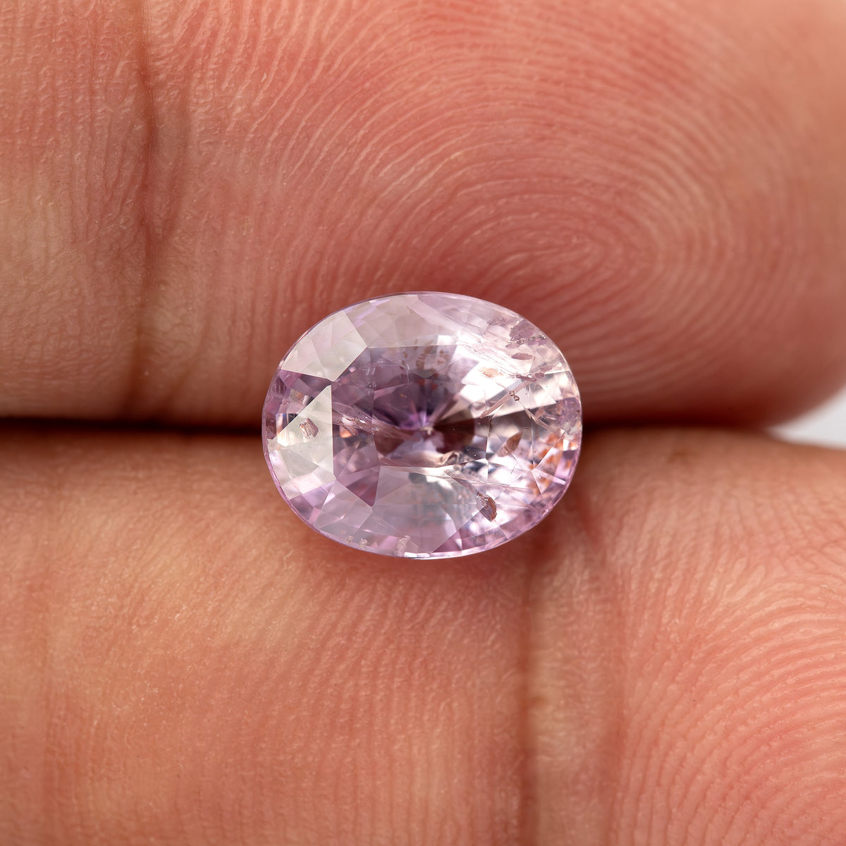 Pink oval sapphire on fingertips at a slightly different face-up angle, with its full outline visible.