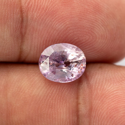 Pink oval sapphire on fingertips at a slightly different face-up angle, with its full outline visible.