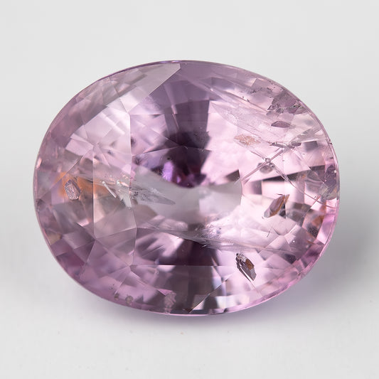 Close face-up view of the pink oval sapphire on white, clearly showing its crown facets and visible natural inclusions.