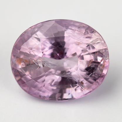 A second close face-up angle of the pink oval sapphire on white, showing the same prominent included features.