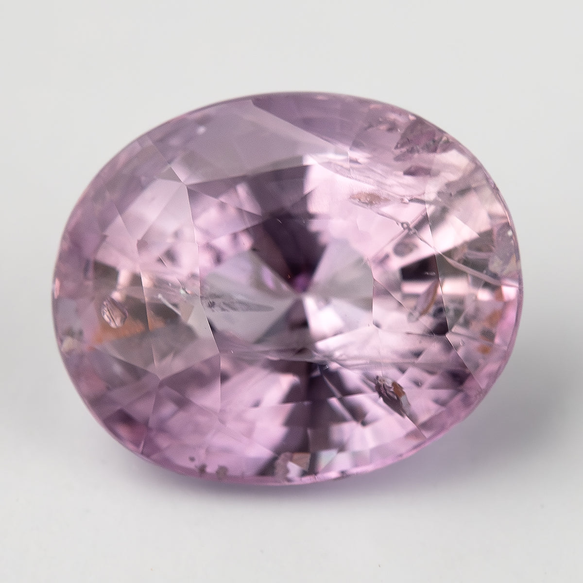 The pink oval sapphire face-up from a diagonal angle, with dark central reflections and brown inclusion details visible.