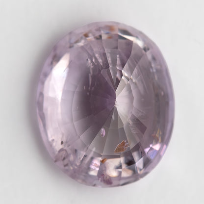 The pink oval sapphire from the opposite side at a diagonal angle, showing intersecting facet reflections and visible inclusions.
