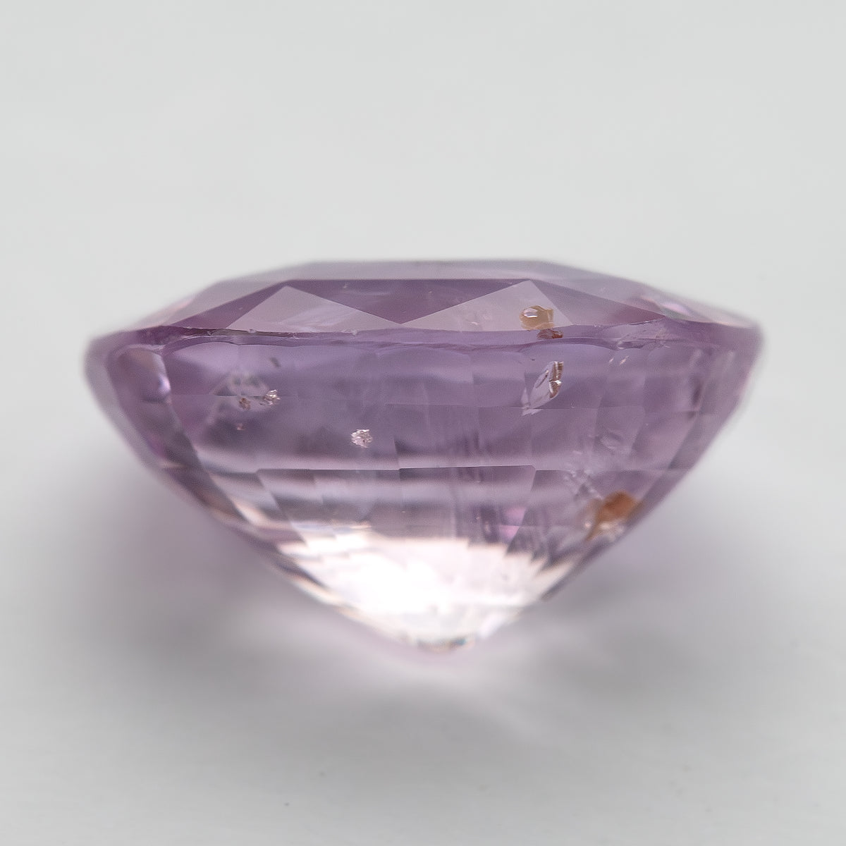 The pink oval sapphire from a second low side angle, with the pavilion tip and inclusion details visible.