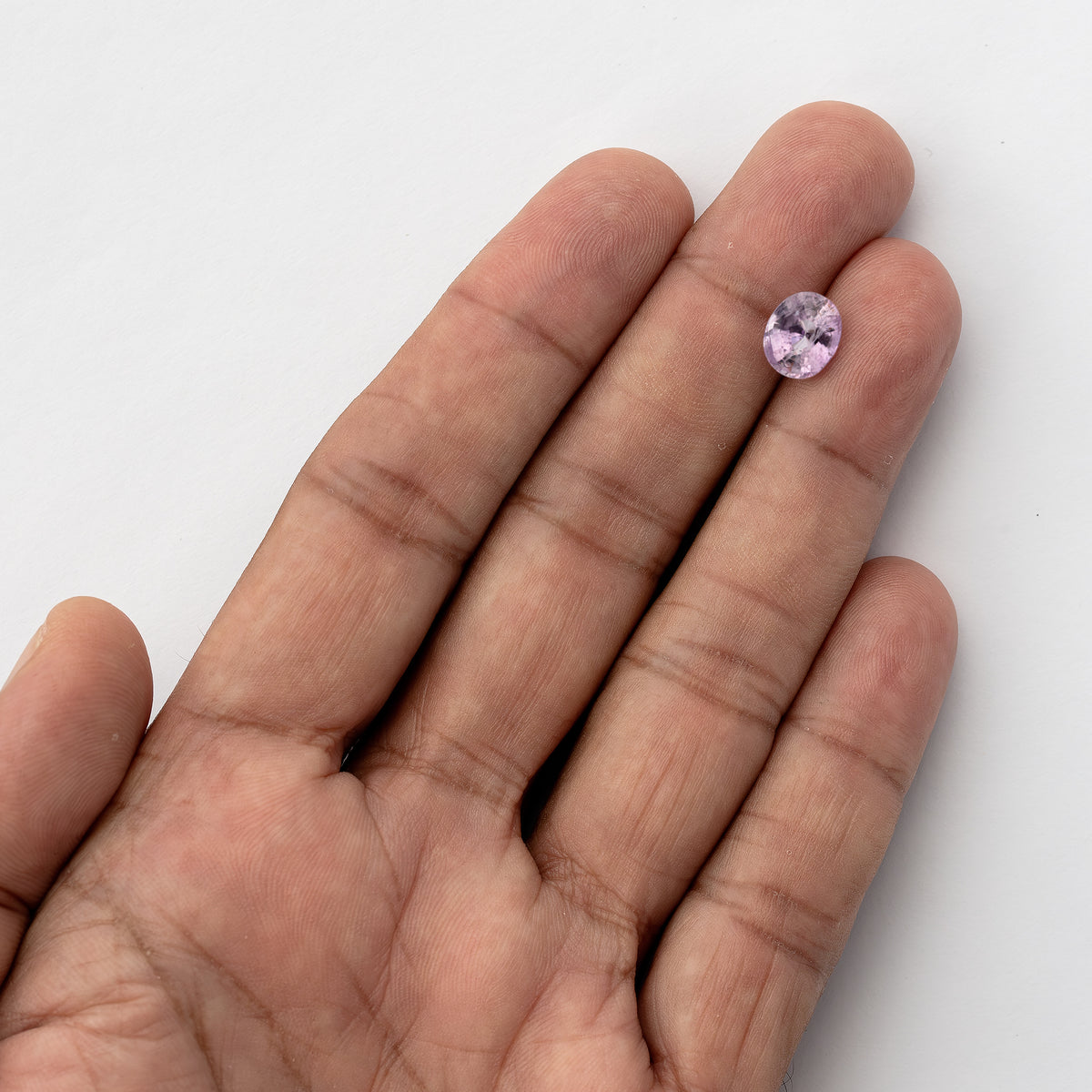 Pink oval sapphire resting on an outstretched finger in a wider hand view, showing its scale.