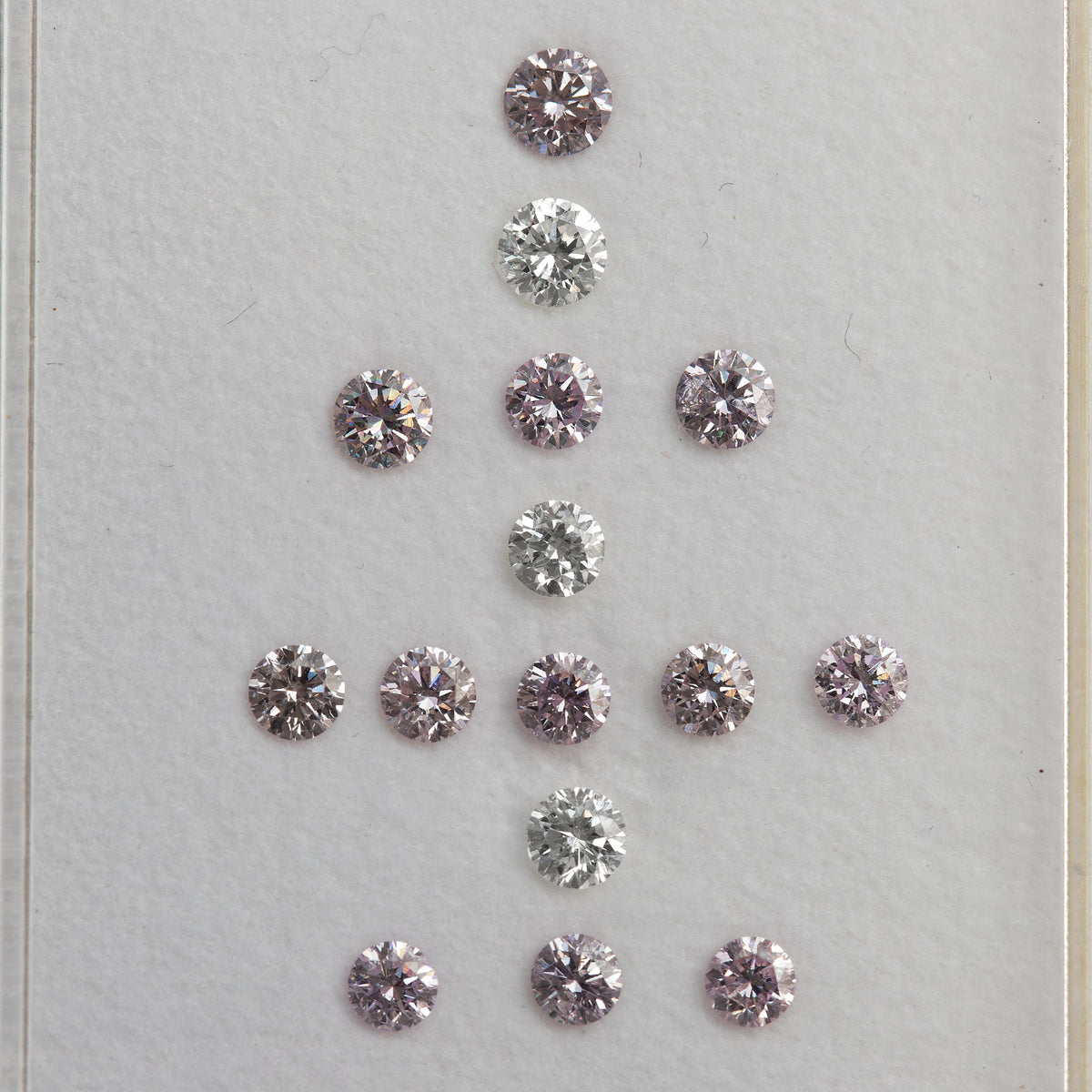 Face-up arrangement of twelve purple-pink diamonds with three white comparison diamonds on a white surface.
