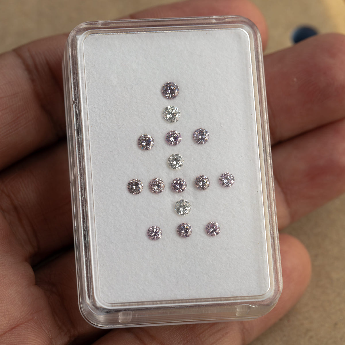 Hand-held box containing twelve purple-pink diamonds and three white comparison diamonds.