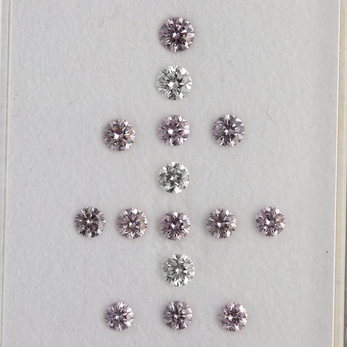Alternate face-up arrangement of twelve purple-pink diamonds with three white comparison diamonds on a white surface.