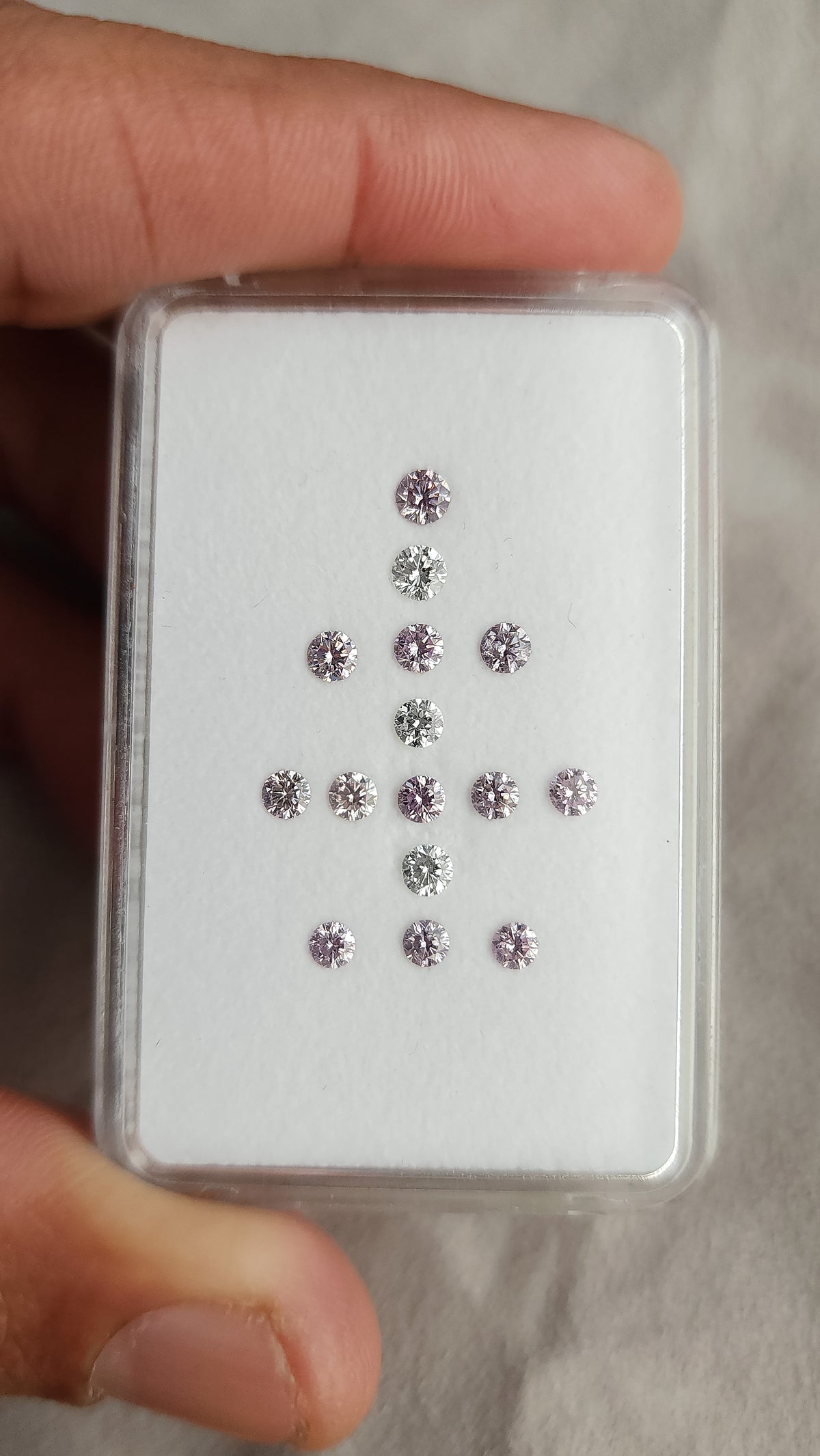 Top-down view of twelve purple-pink diamonds and three white comparison diamonds in a display box.