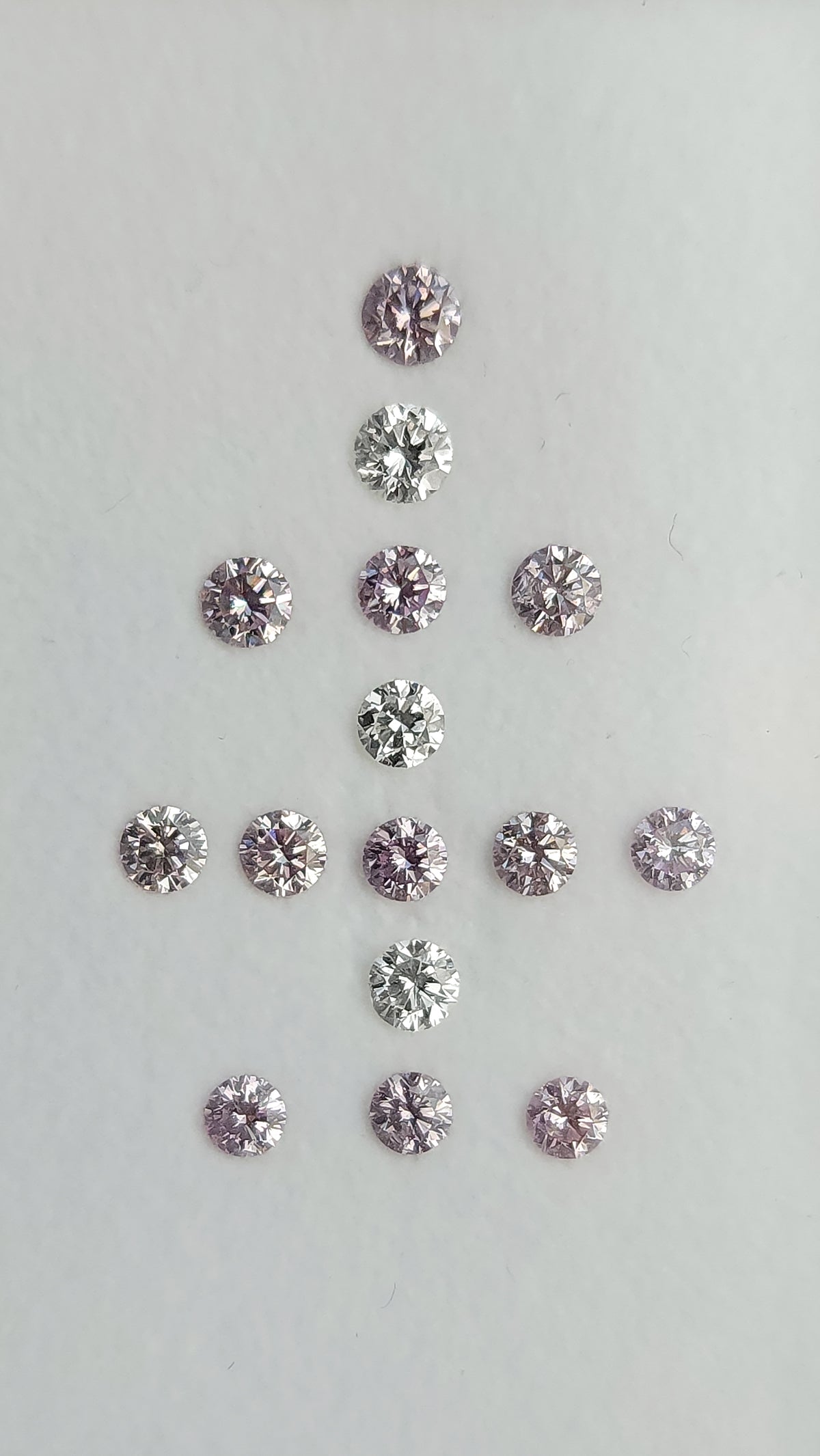 Face-up arrangement of twelve purple-pink diamonds and three white comparison diamonds on a neutral background.