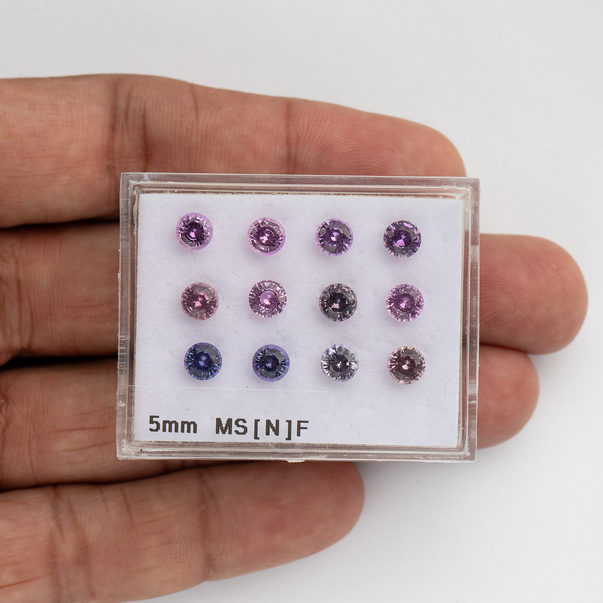 12個のラウンドファセットカットサファイアが入ったプラスチック製ディスプレイボックスを手に持った様子。