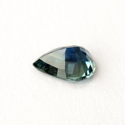 Pale blue-green pavilion of the pear-shaped sapphire resting on white at an oblique angle.
