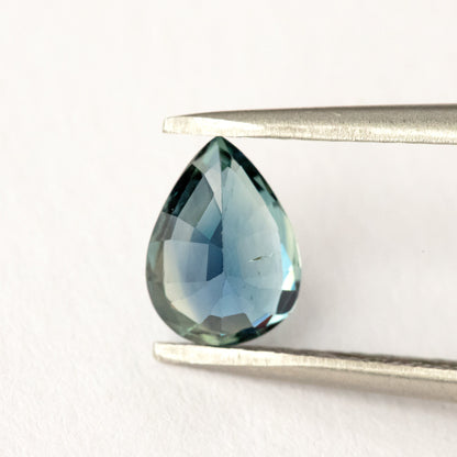 Back view of the pear-shaped sapphire held in tweezers, showing broad pale blue-green pavilion facets.