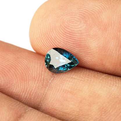 Pear-shaped sapphire between fingertips with a bright central reflection and blue facets around the edge.