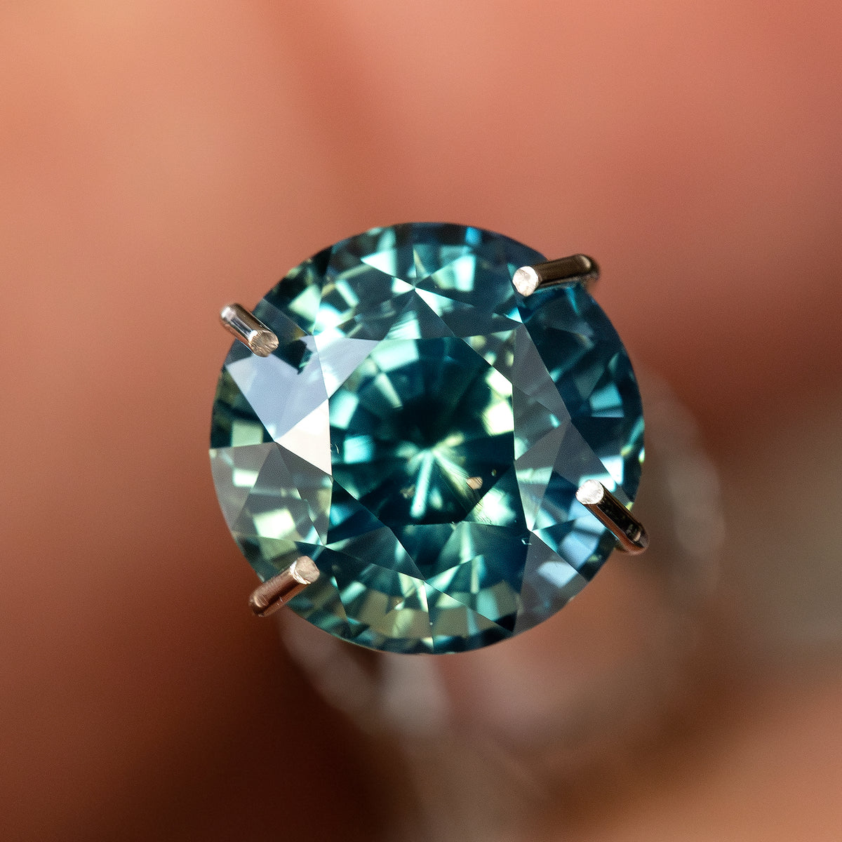 Round teal blue green sapphire face-up in a temporary prong-style inspection holder; the holder is not included.