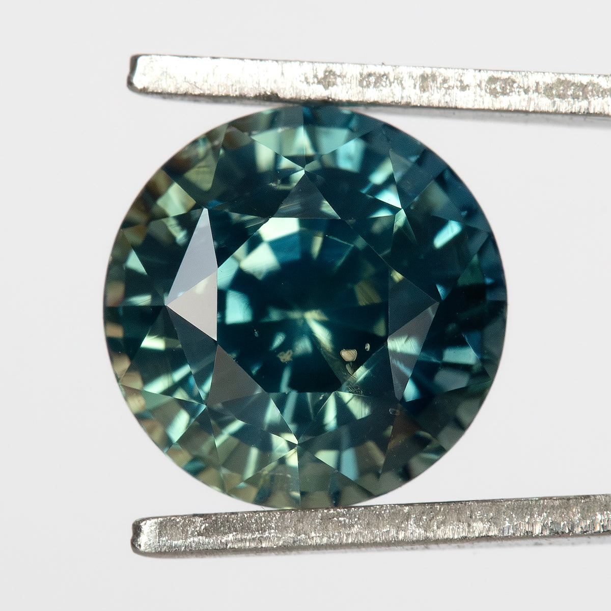 Loose round sapphire held in jeweler's tweezers against a white background.