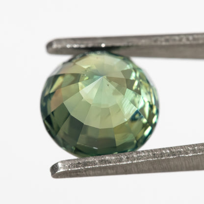 Reverse view of the deep teal blue green sapphire showing pavilion facets in tweezers.